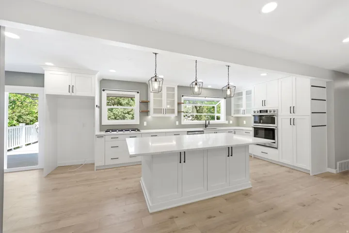 Chef's kitchen featuring white shaker cabinetry, stainless steel built-in appliances, quartz countertops, and a large center island with pendant lighting