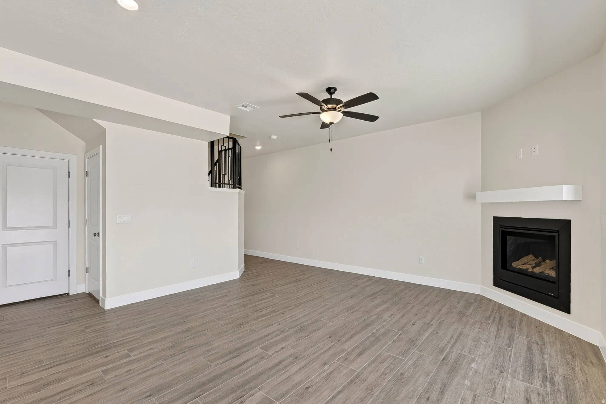Spacious room featuring wood-finish tile flooring, a corner fireplace with a white mantel, and a ceiling fan with integrated lighting