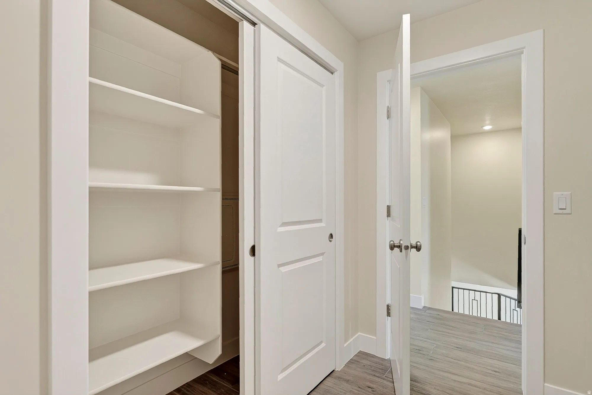 Built-in closet shelving, white interior doors, door hardware with a satin finish, light wall color, and wood-finish flooring