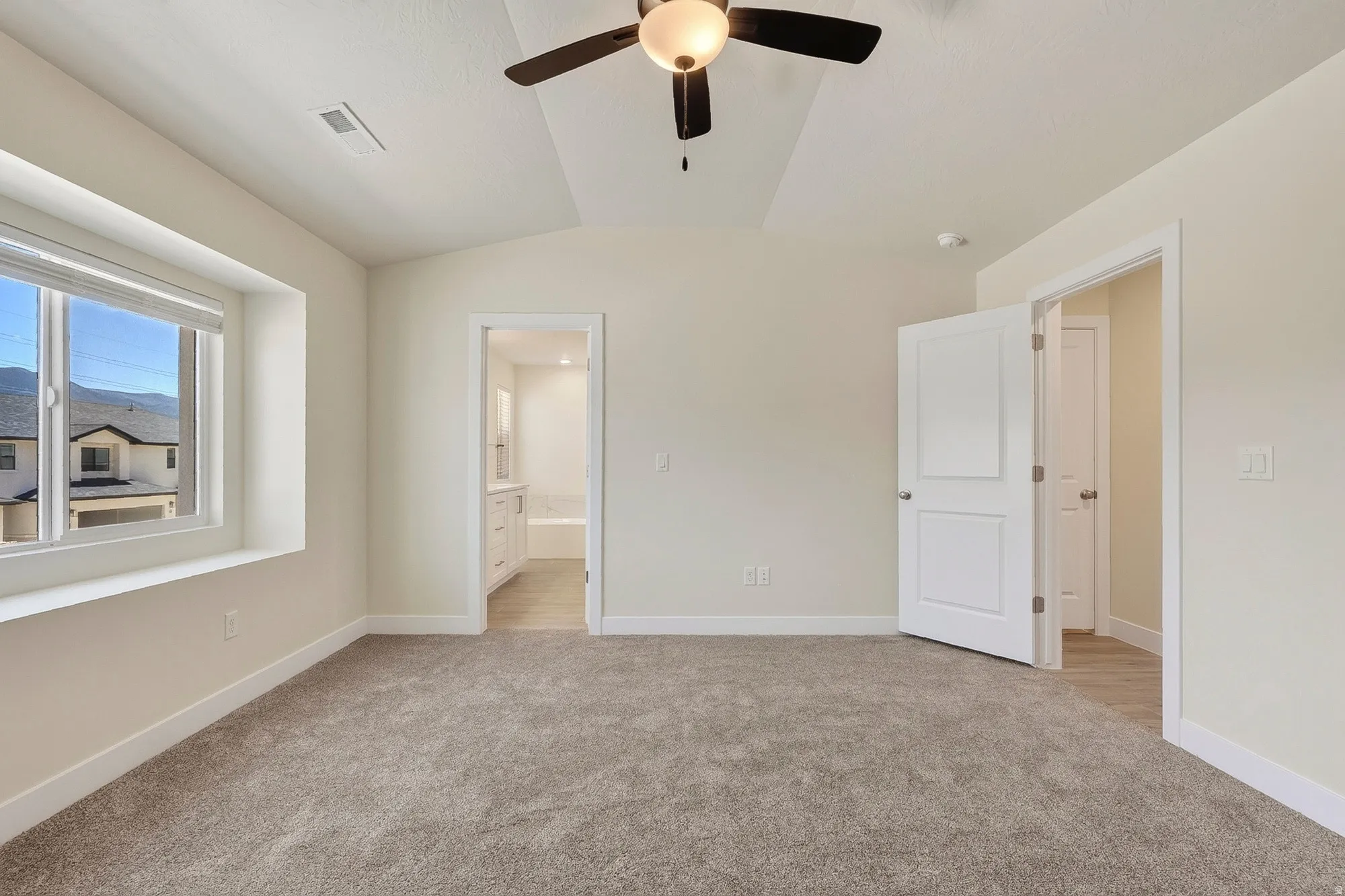 Carpeted room with a ceiling fan, a window with roller shades, and two paneled doors