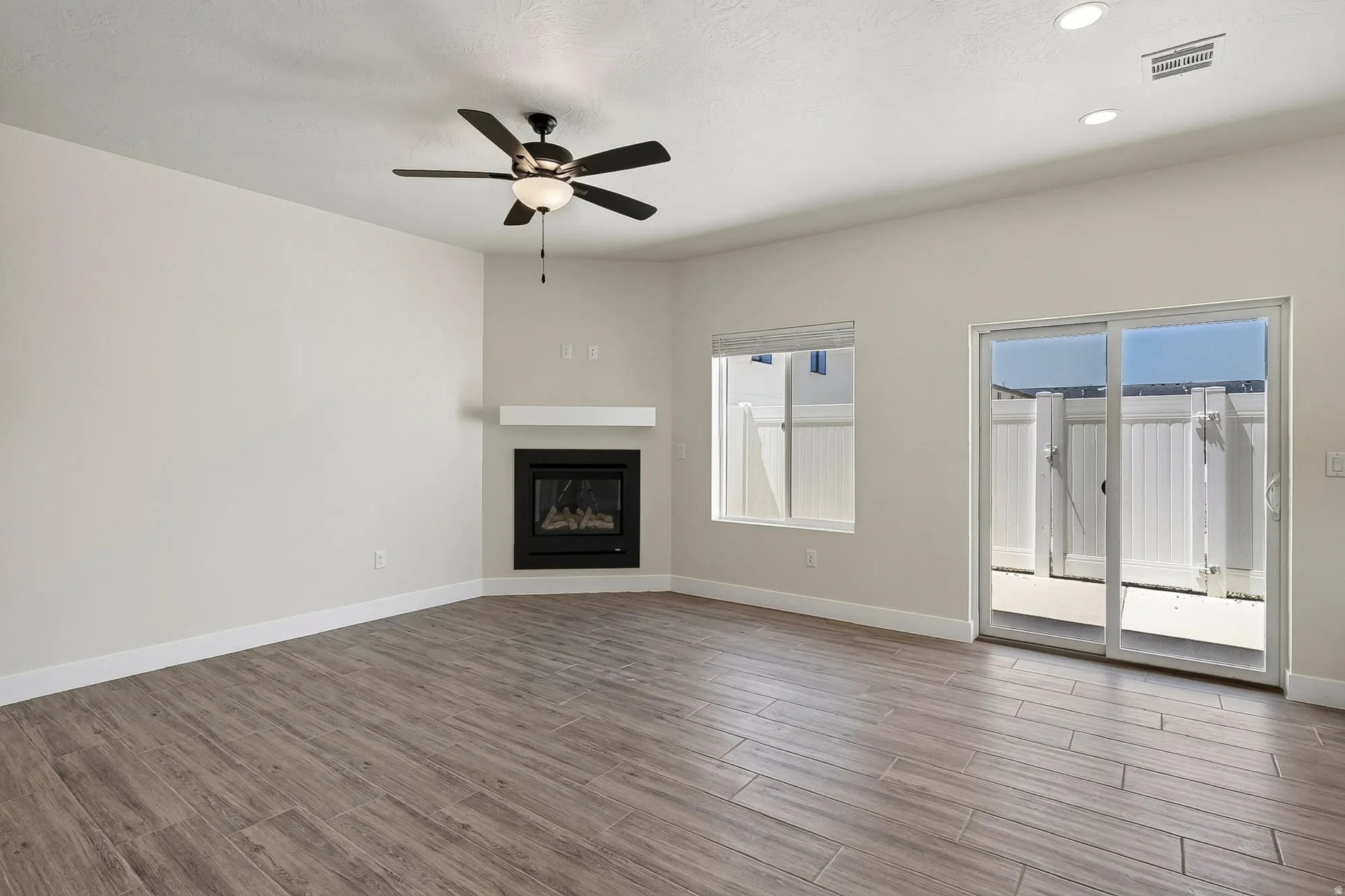 Wood-finish flooring throughout, featuring a corner fireplace with a white mantel, and a ceiling fan with integrated lighting