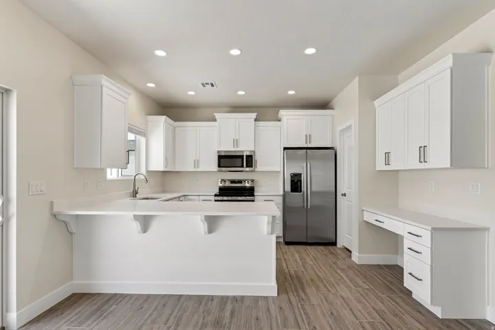 Modern kitchen featuring white shaker cabinetry, stainless steel appliances, a breakfast bar, and wood-finish flooring