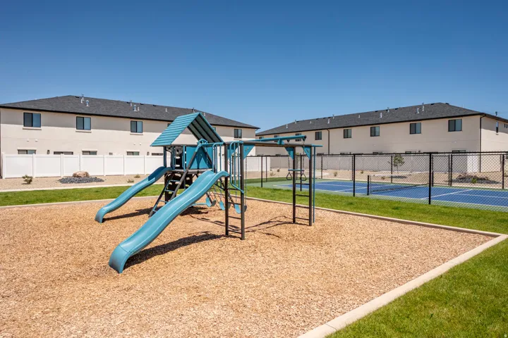 Community playground with a blue and green play structure, wood chip ground cover, and a manicured lawn