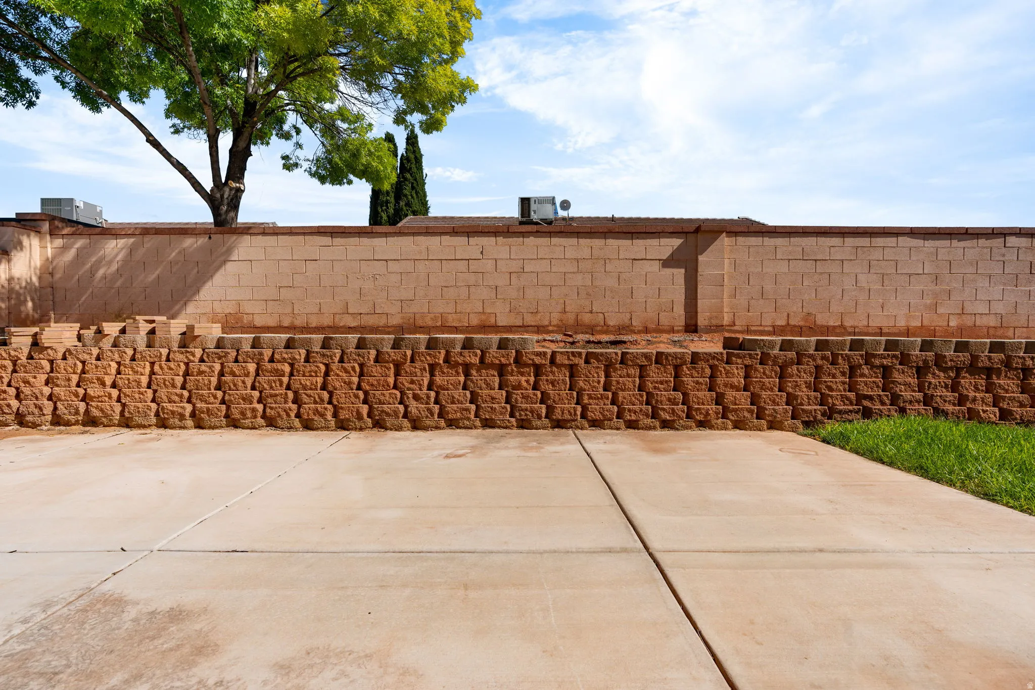 Expansive concrete patio with a retaining wall and mature landscaping