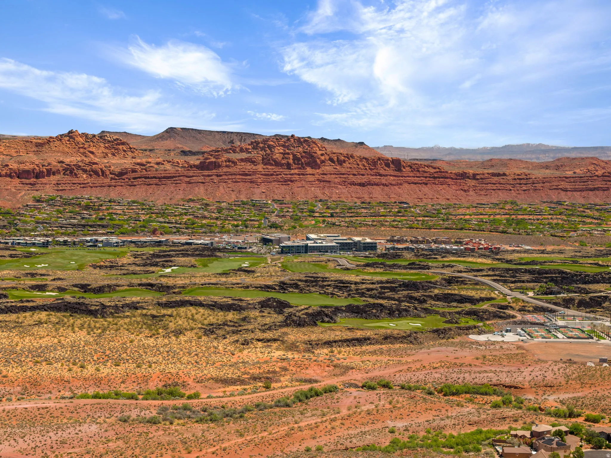 Expansive desert landscape with red rock formations, green golf course fairways, and residential structures