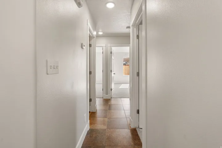 Recessed lighting illuminates the hallway with white walls and a tiled floor