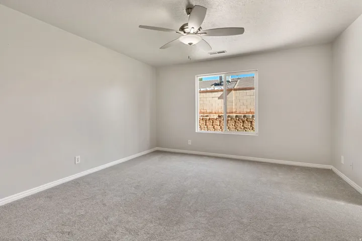 Spacious room featuring neutral carpeting, light-toned wall paint, a ceiling fan with integrated lighting, and a large window