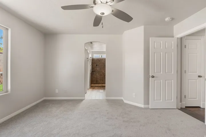 Plush carpeting, ceiling fan with integrated lighting, arched doorway, six-panel interior doors, and a window providing natural light