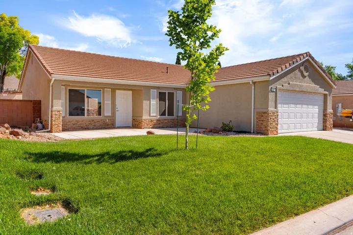 Stucco exterior with stone accents, a tiled roof, an attached two-car garage, an expansive lawn, and a concrete driveway