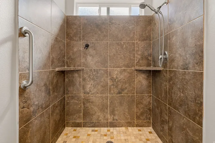 Tiled shower with a handheld showerhead, two built-in storage shelves, and a window