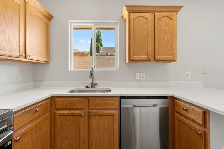 U-shaped kitchen layout featuring wood cabinetry, light-toned countertops, a stainless steel sink with a gooseneck faucet, and a built-in stainless steel dishwasher