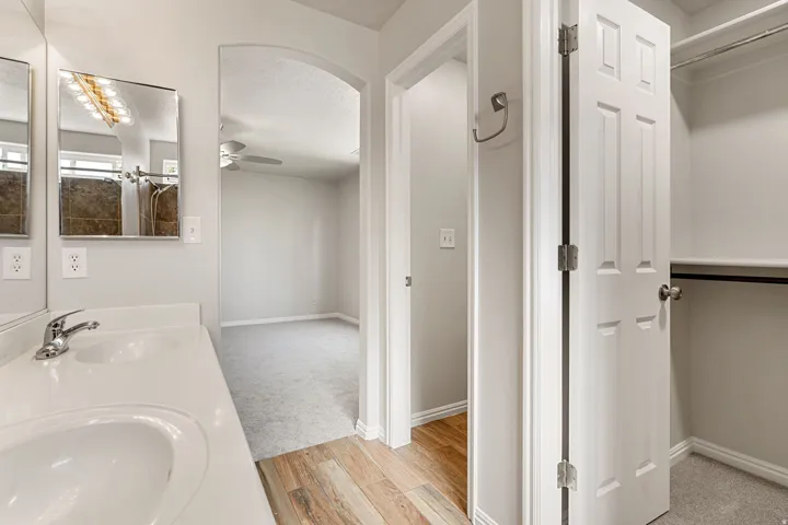 Dual vanity with integrated sinks, wood-finish flooring, arched doorway, and a walk-in closet with built-in shelving