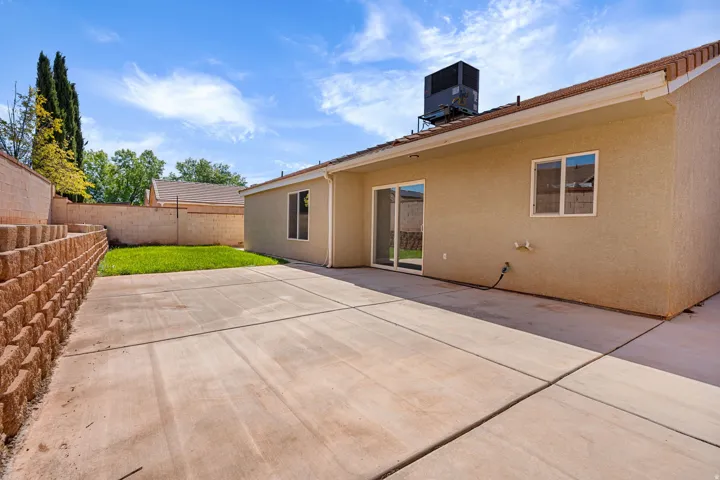 Expansive concrete patio with a retaining wall, green lawn section, and sliding glass door access