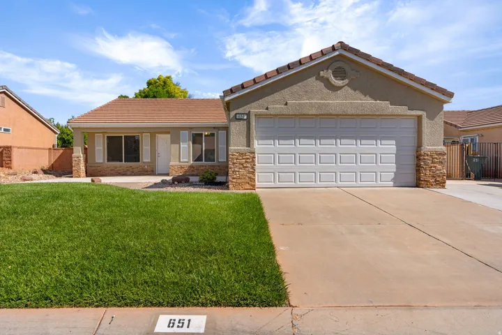 Stucco exterior with stone accents, attached garage, covered entry, and a concrete driveway