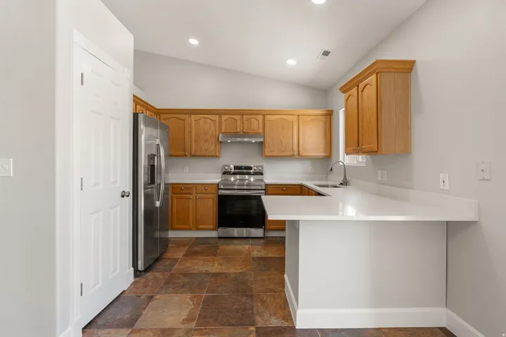 Kitchen featuring light wood cabinetry, stainless steel appliances, a white solid surface countertop, and multi-toned tile flooring