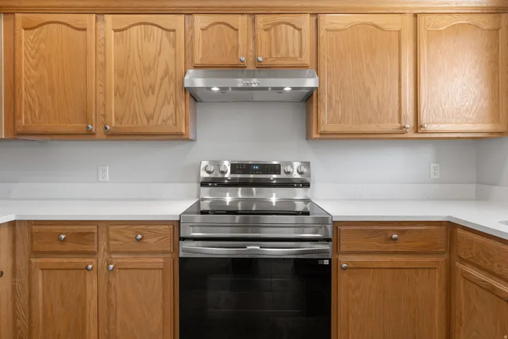Full kitchen featuring light wood cabinetry, a stainless steel range with an overhead exhaust hood, and white countertops