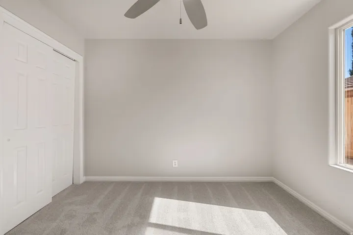 Neutral tone wall paint, light gray carpet flooring, white trim, recessed closet with bi-fold doors, and a ceiling fan