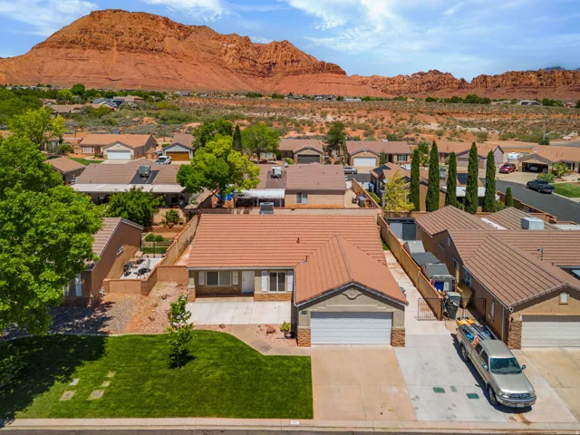 Tile roof, attached garage, concrete driveway, mature landscaping, and a red rock mountain backdrop