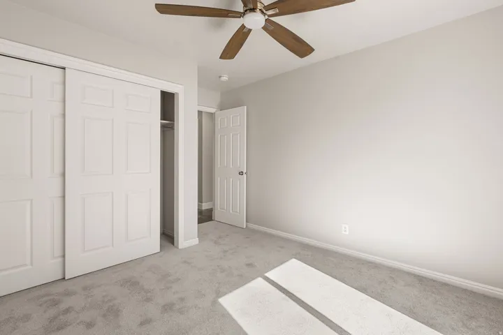 Neutral tone wall paint, carpeted flooring, ceiling fan with wood-finish blades, and sliding closet doors