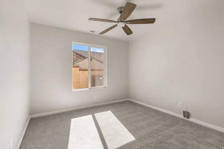 Bright secondary bedroom featuring neutral carpeting, ceiling fan with integrated lighting, and large window with natural light exposure