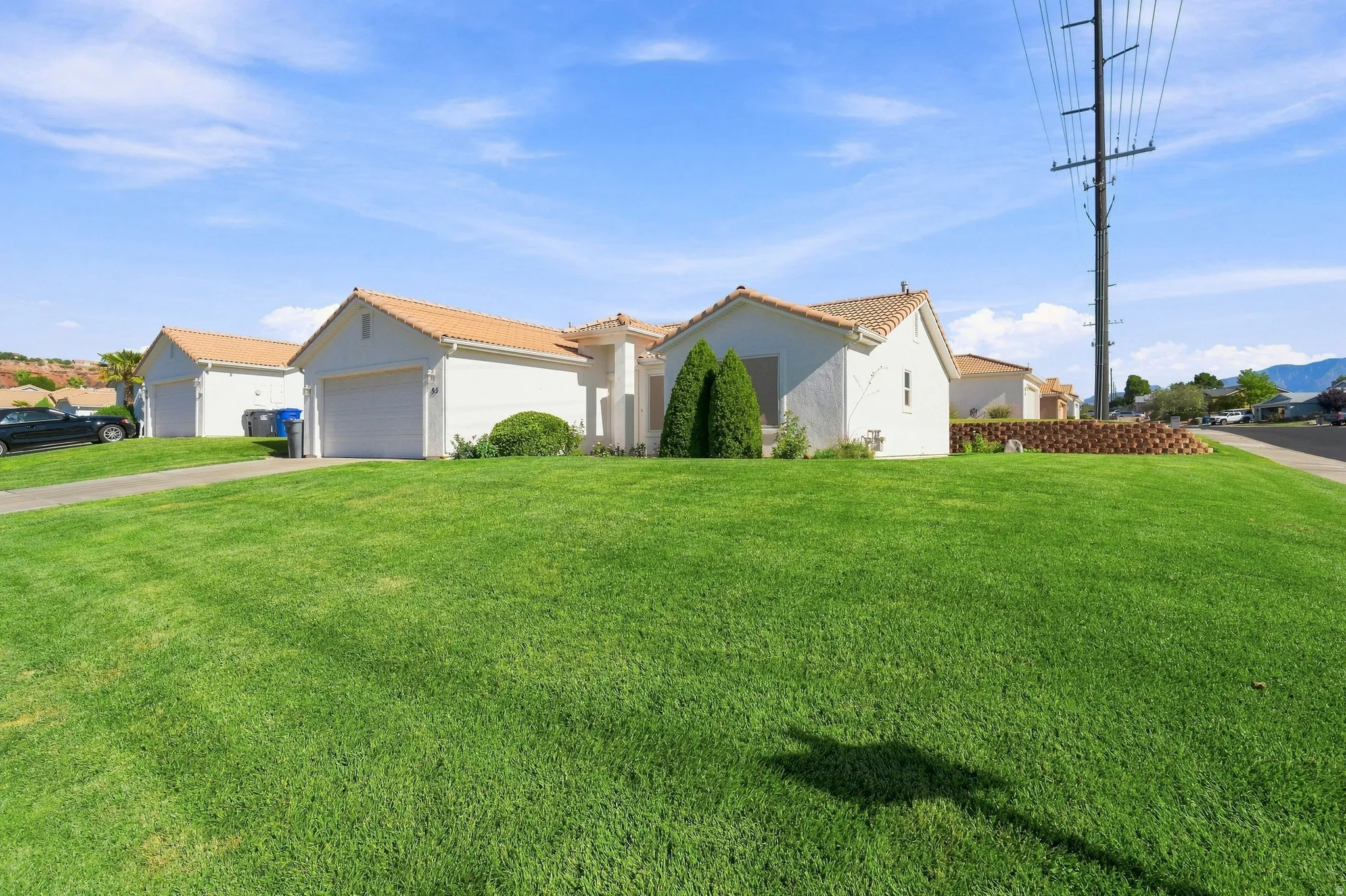 White stucco exterior with a terracotta tile roof, featuring an attached garage, a verdant front lawn, and foundational landscaping