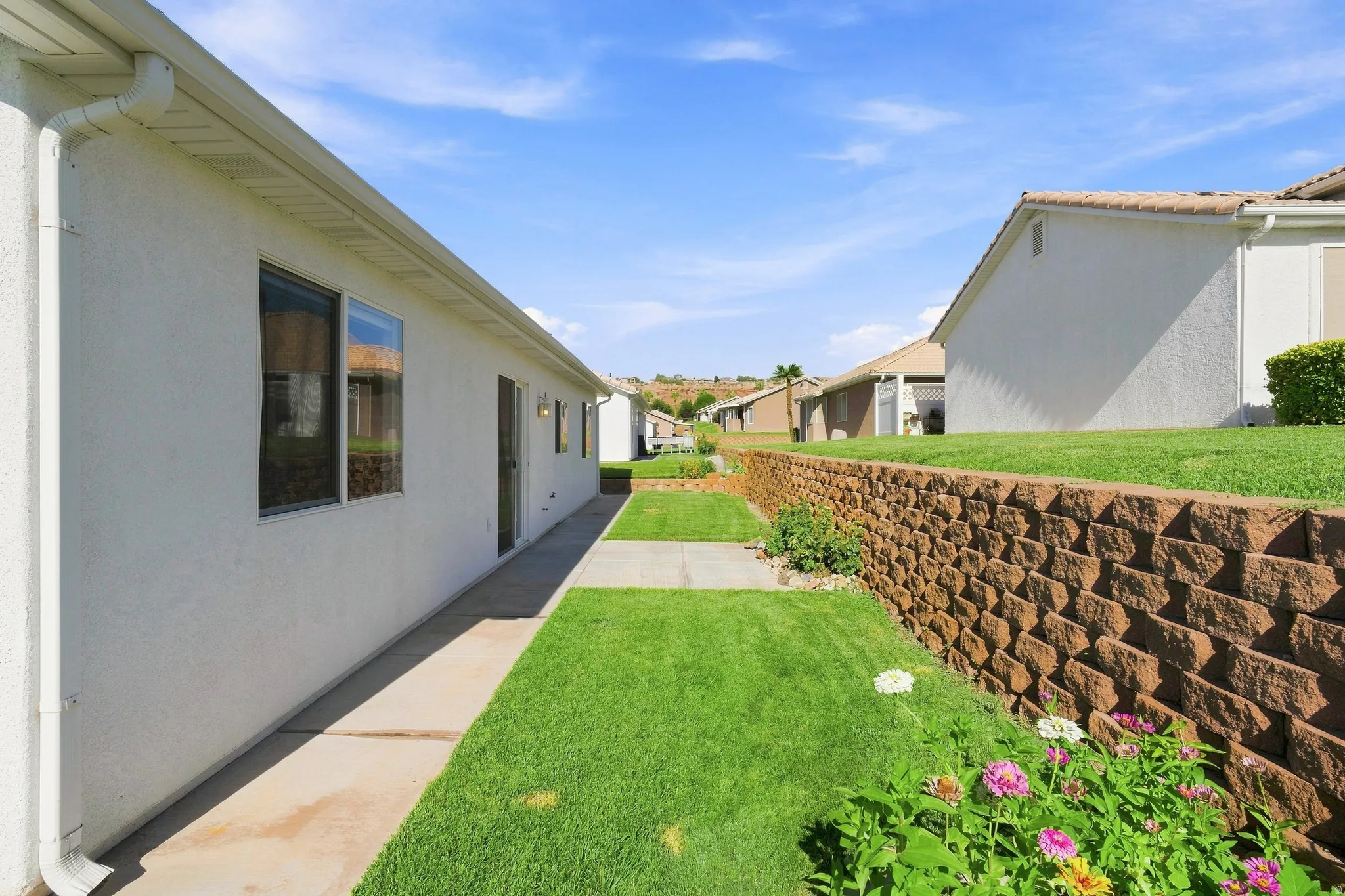 Side yard featuring a concrete walkway, expansive green lawn, and a stacked stone retaining wall