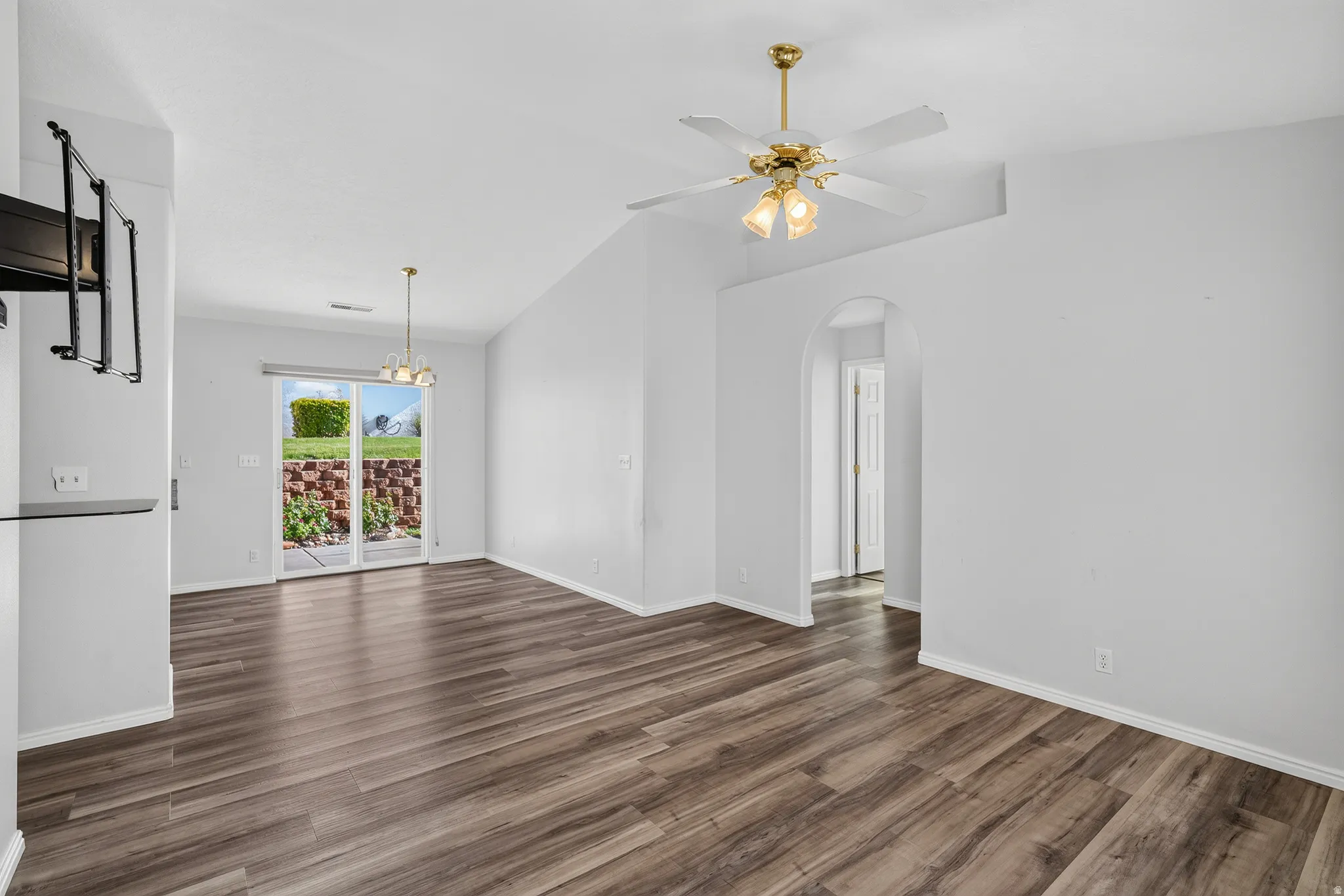 Spacious open-concept living area showcasing wide-plank wood-finish flooring, white walls, and abundant natural light from glass doors