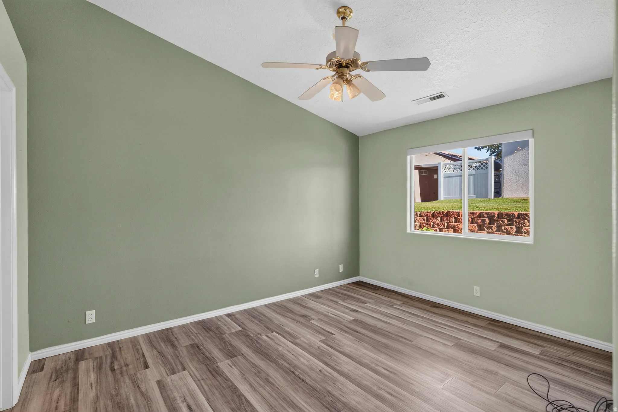Spacious bedroom featuring soft sage-green walls, wood-finish flooring throughout, recessed lighting, and a ceiling fan with brass accents