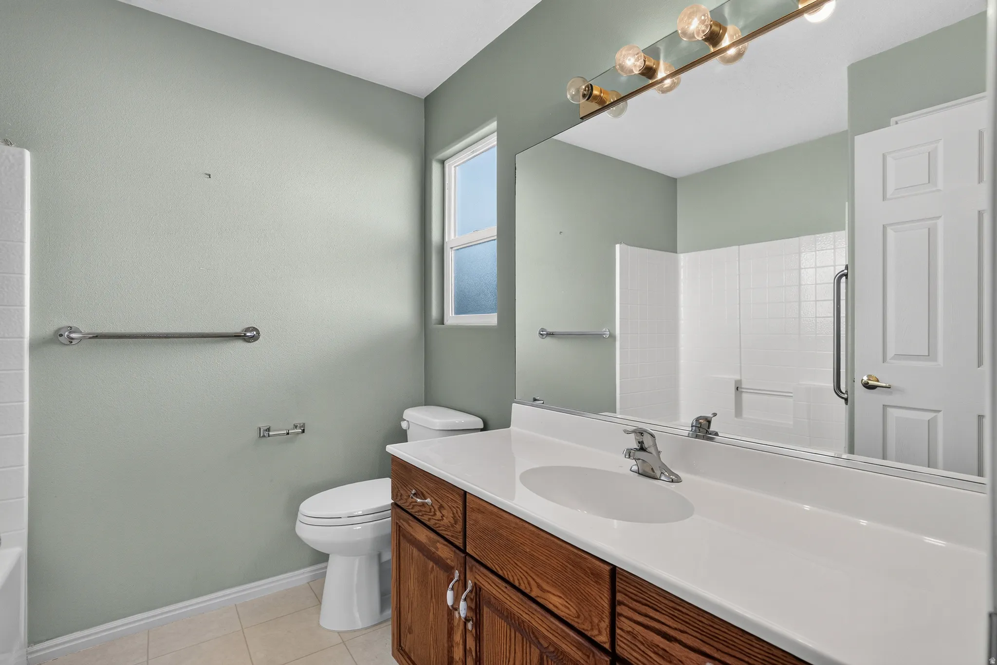 Bathroom featuring a wood-finish vanity with a white countertop and integrated sink, a large wall-mounted mirror, and a gold-tone vanity light fixture
