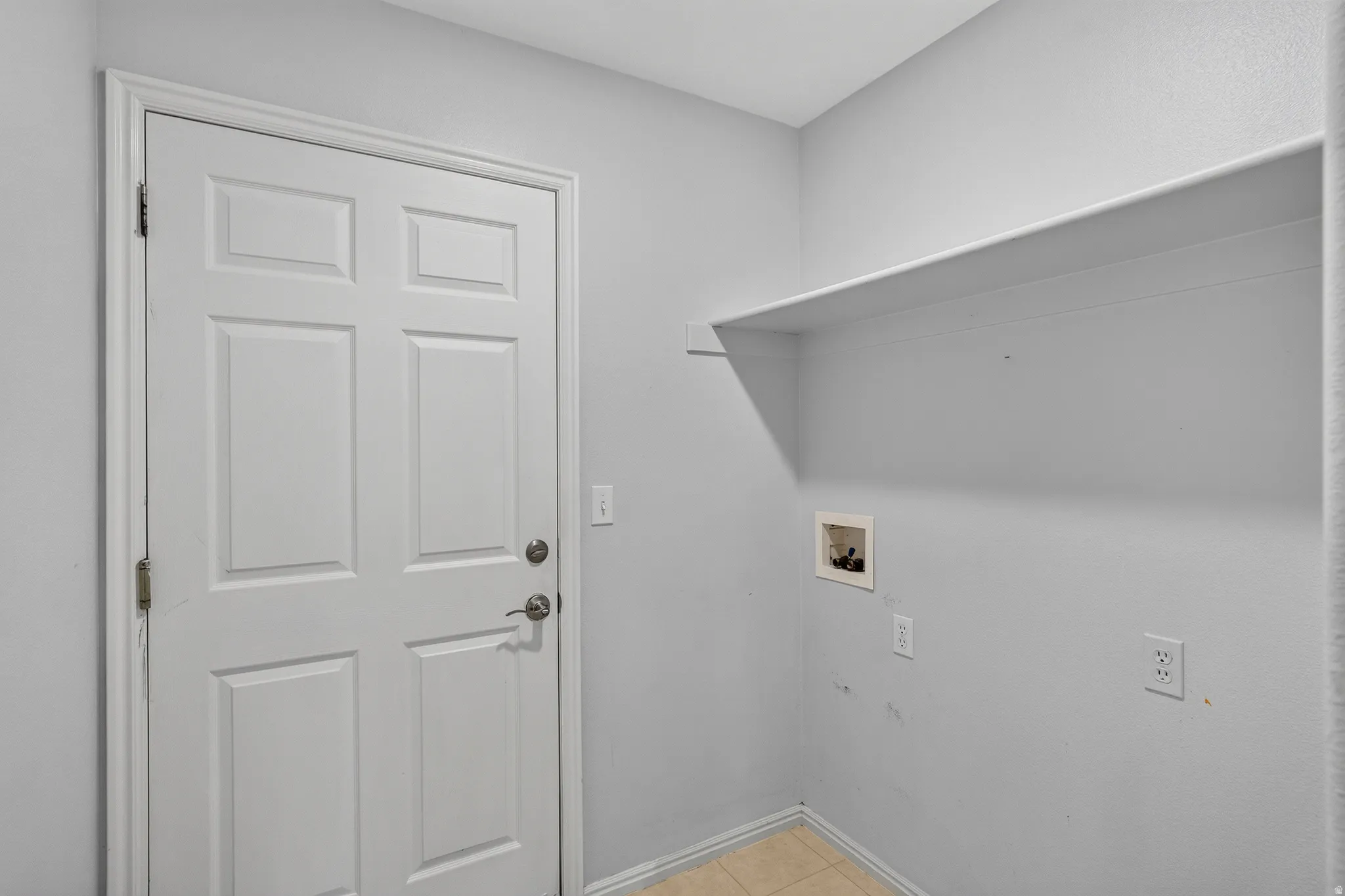 Utility space featuring a six-panel door, wall-mounted shelving, and utility hookups