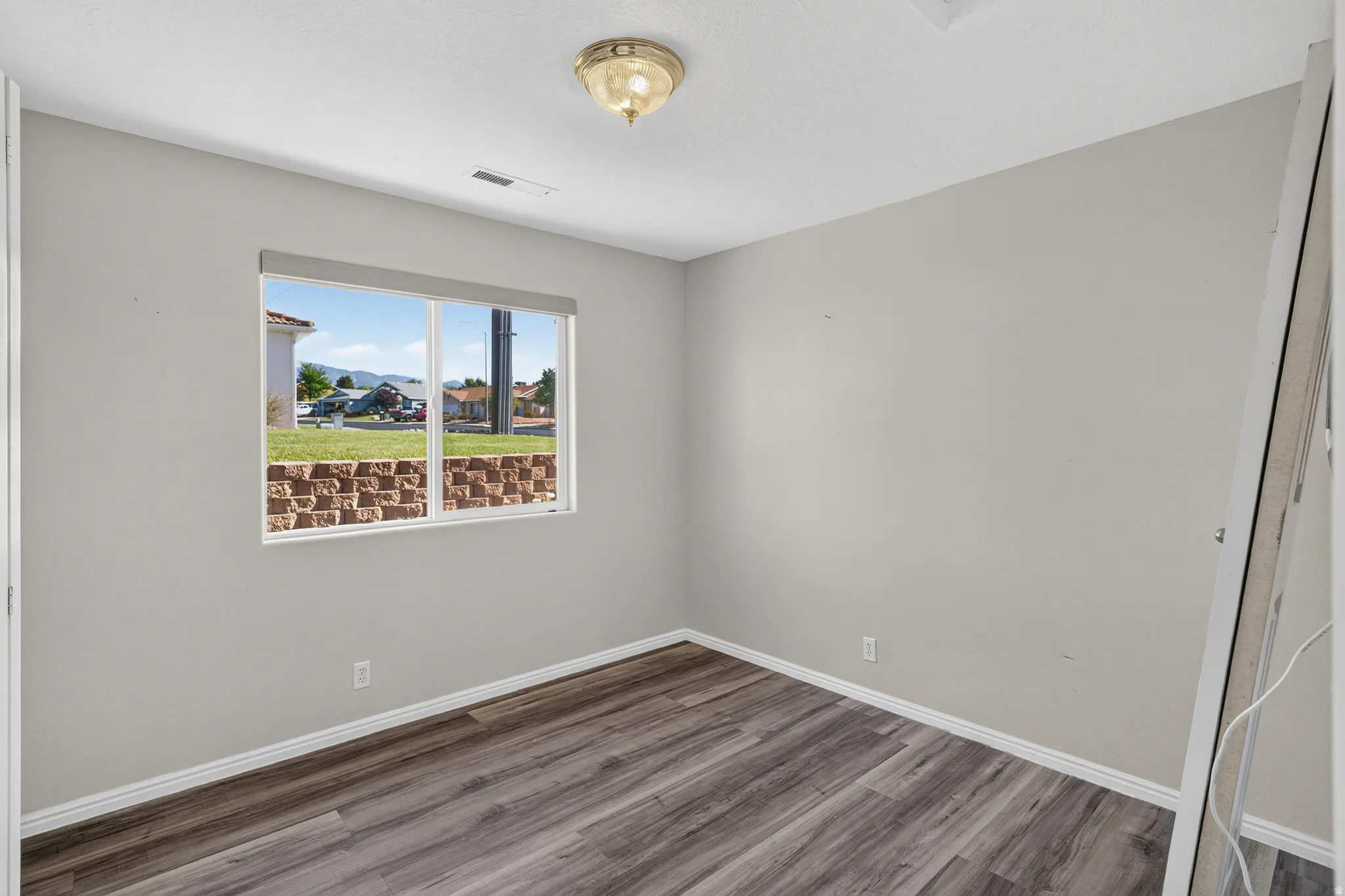 Bright bedroom featuring large picture window with natural light, neutral wall finishes, and wood-finish flooring throughout