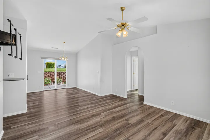 Spacious open-concept living area showcasing wide-plank wood-finish flooring, white walls, and abundant natural light from glass doors