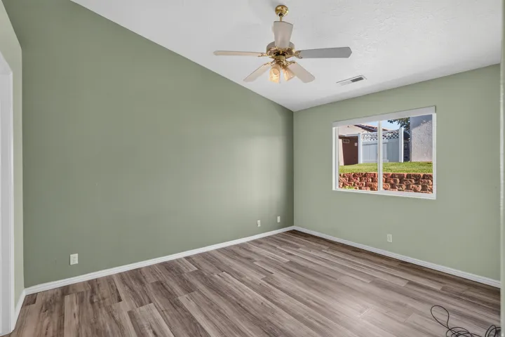 Spacious bedroom featuring soft sage-green walls, wood-finish flooring throughout, recessed lighting, and a ceiling fan with brass accents