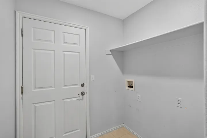 Utility space featuring a six-panel door, wall-mounted shelving, and utility hookups