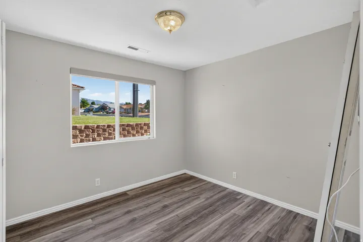 Bright bedroom featuring large picture window with natural light, neutral wall finishes, and wood-finish flooring throughout