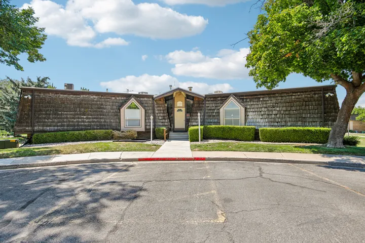 Contemporary single-story residence featuring a distinctive wood-shake exterior with architectural detailing, centered entry portico with decorative trim, and manicured landscaping anchored by mature specimen trees