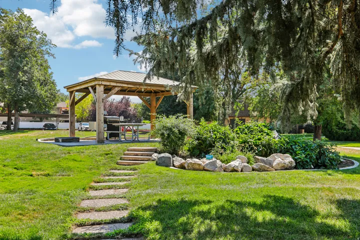Expansive green space featuring a wooden gazebo with a metal roof, a stone-stepped pathway, and established landscaping with natural rock accents