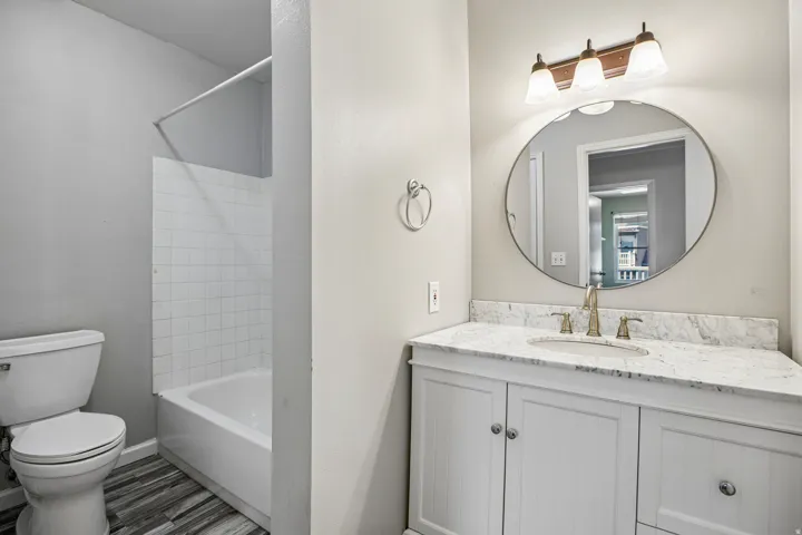 White vanity with a stone countertop, an undermount sink, and a circular mirror