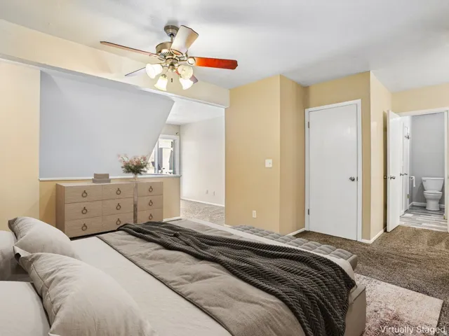Carpeted room featuring a ceiling fan with integrated lighting, a white panel door, and an opening to an additional space