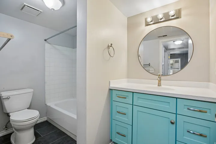Bathroom featuring a turquoise vanity with a white countertop, a circular mirror, and a vanity light fixture