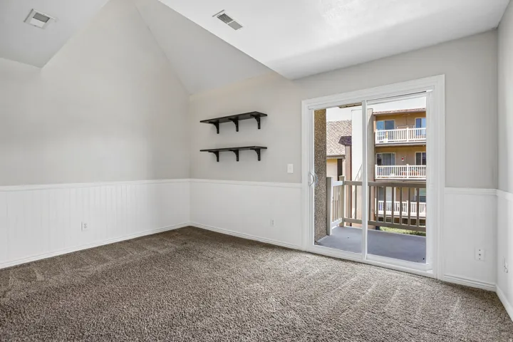 Vaulted ceiling, wainscoting, built-in shelving, sliding glass door, and private balcony
