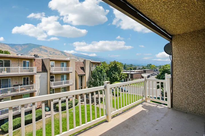 Pebble-dash exterior balcony with a white railing and concrete flooring overlooking a residential area with mountains in the background