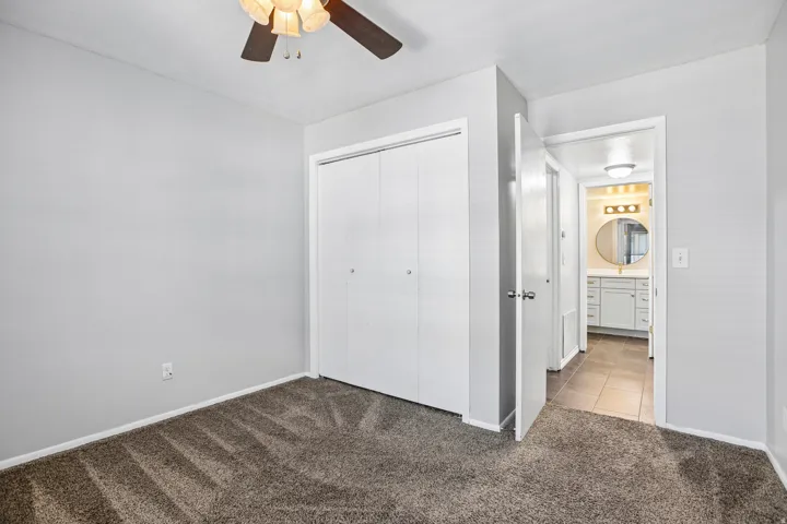 Spacious bedroom with neutral wall finishes, carpeted flooring, ceiling fan with integrated lighting, and dual closets with white bi-fold doors
