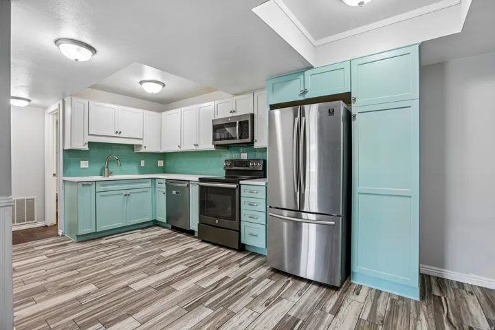 Kitchen featuring two-tone cabinetry with upper white and lower teal finishes, a teal tile backsplash, and stainless steel appliances