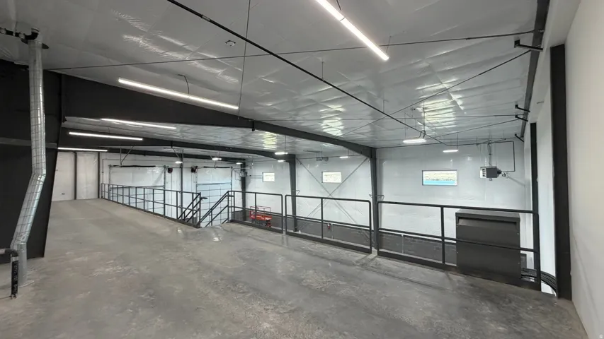Concrete flooring with a sloped entry, metal railing, and exposed ceiling with linear fluorescent lighting