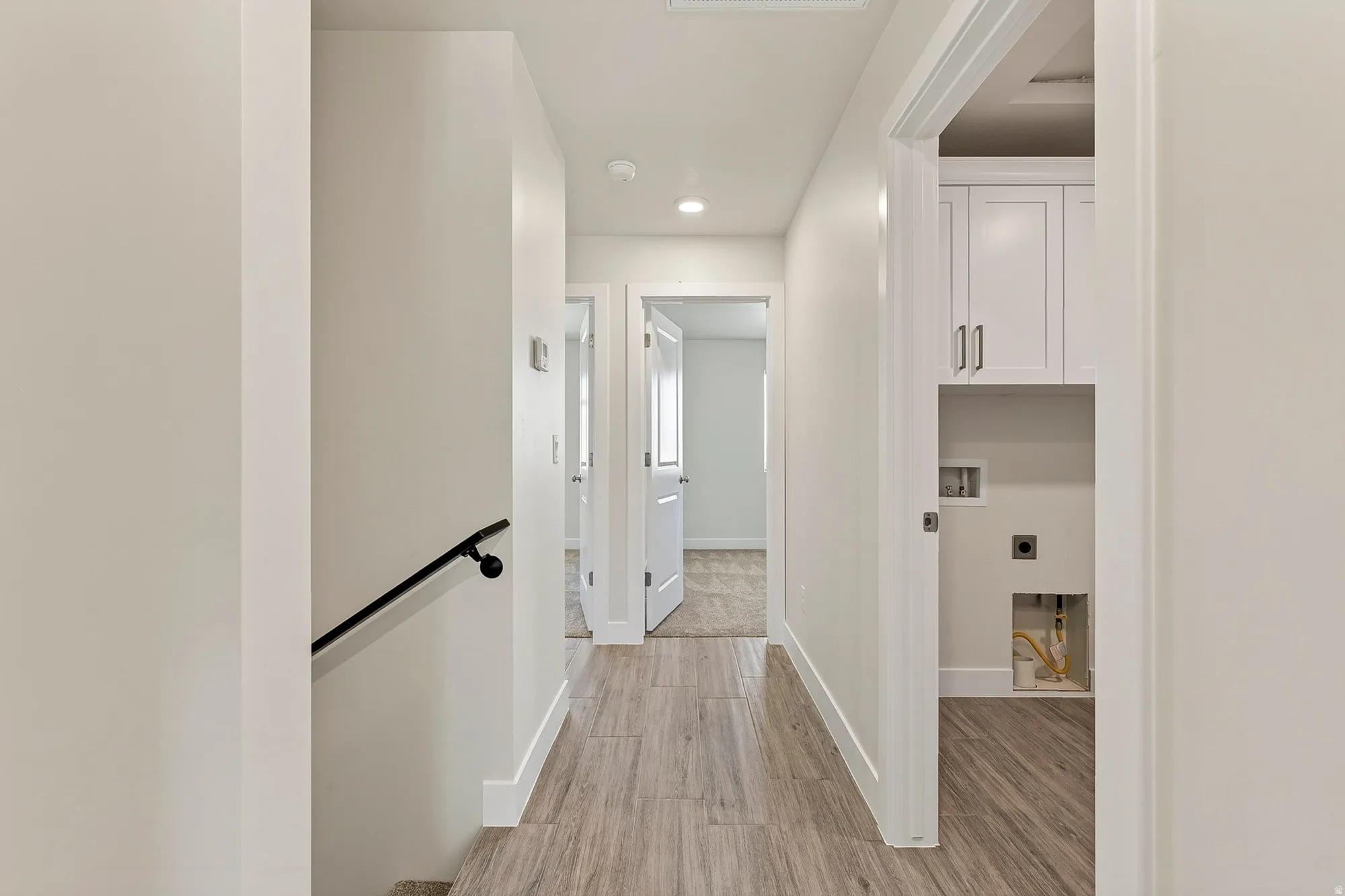 Hallway featuring wood-finish flooring, recessed lighting, and a built-in laundry area with cabinetry