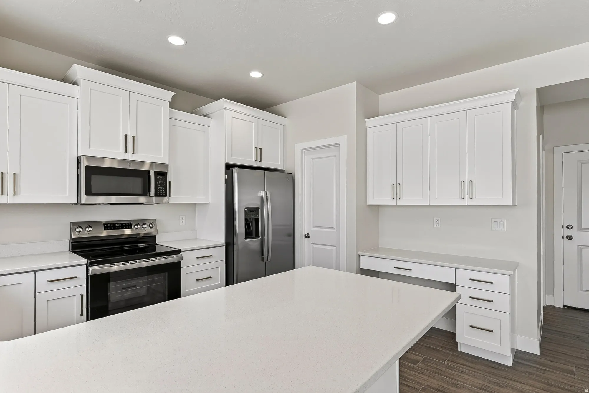 Modern kitchen featuring white shaker cabinetry, stainless steel appliances, a large center island, and wood-finish flooring