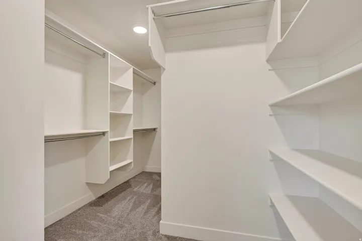 Built-in shelving, multiple hanging rods, recessed ceiling lighting, and soft carpet flooring