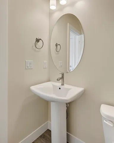 Pedestal sink with a single-handle faucet, oval mirror, and wall-mounted light fixture