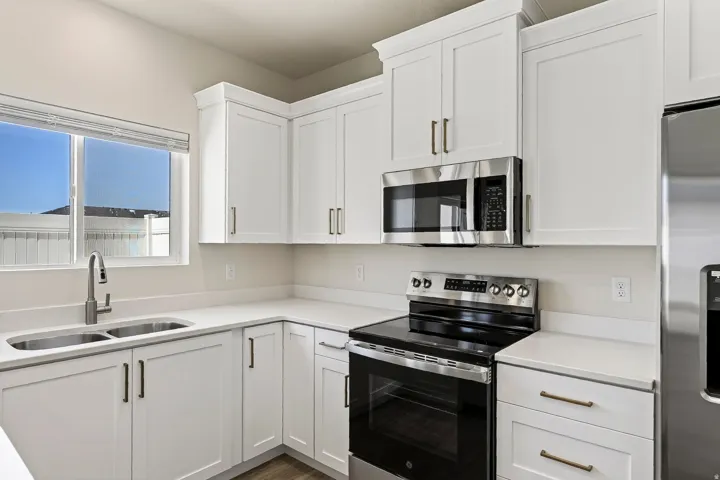 Kitchen featuring white cabinetry, stainless steel appliances, a double basin sink, and light-toned countertops